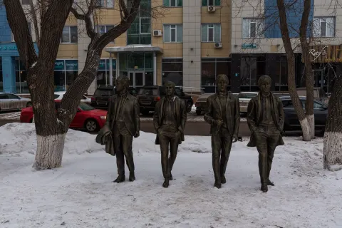 Four life-size standing Beatles figures in long coats on a snowy pavement on the Arbat pedestrian zone in Astana, February 2019