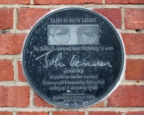Round black plaque to Julia Lennon and John Lennon on the brick wall of the former Liverpool Maternity Hospital, Liverpool