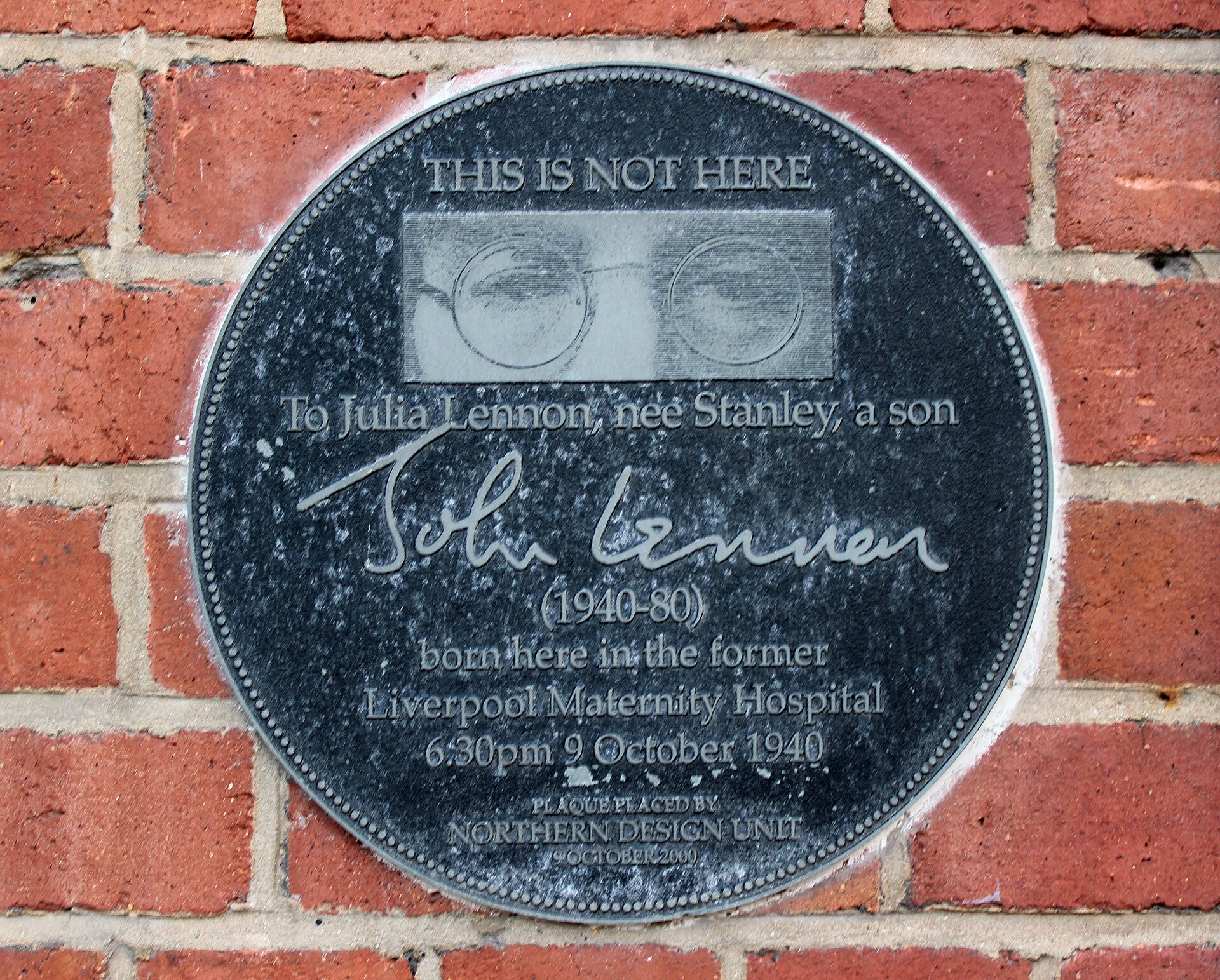 Round black plaque to Julia Lennon and John Lennon on the brick wall of the former Liverpool Maternity Hospital, Liverpool