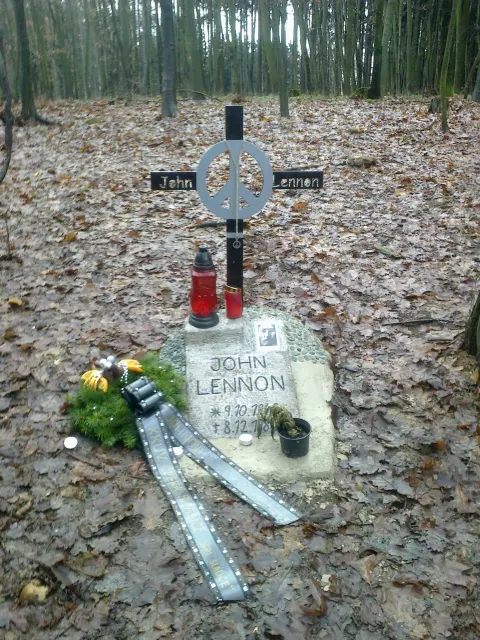 John Lennon memorial in the woods at Česká Skalice: a metal cross with a peace sign and a stone inscribed JOHN LENNON, with candles and a wreath