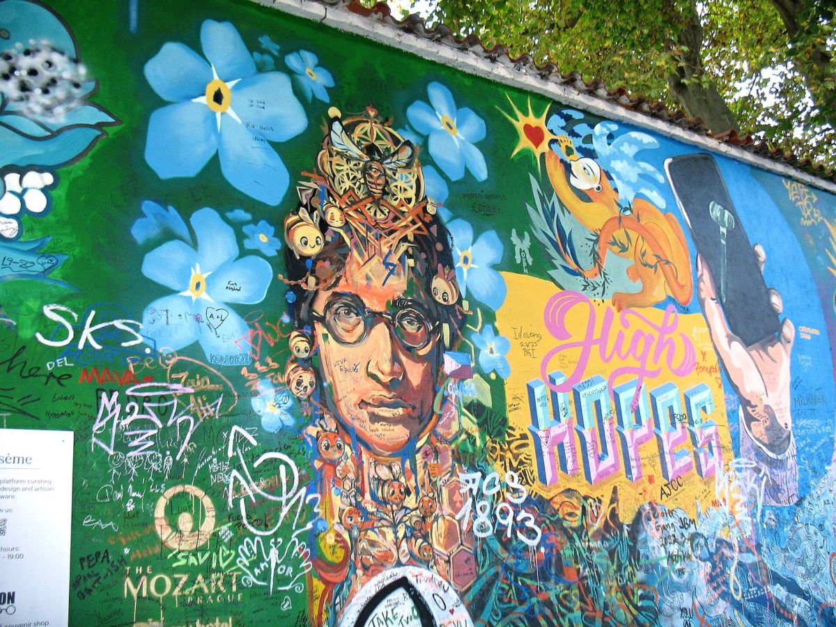 Painted portrait of John Lennon among blue flowers and visitors' writing on the Lennon Wall in Prague, October 2022