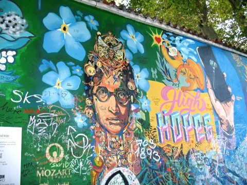 Painted portrait of John Lennon among blue flowers and visitors' writing on the Lennon Wall in Prague, October 2022