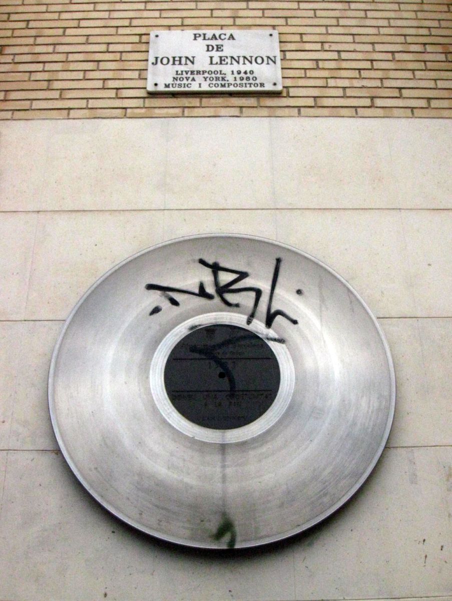 Record-shaped metal disc and marble street sign on a wall of Placa de John Lennon in Gracia, Barcelona
