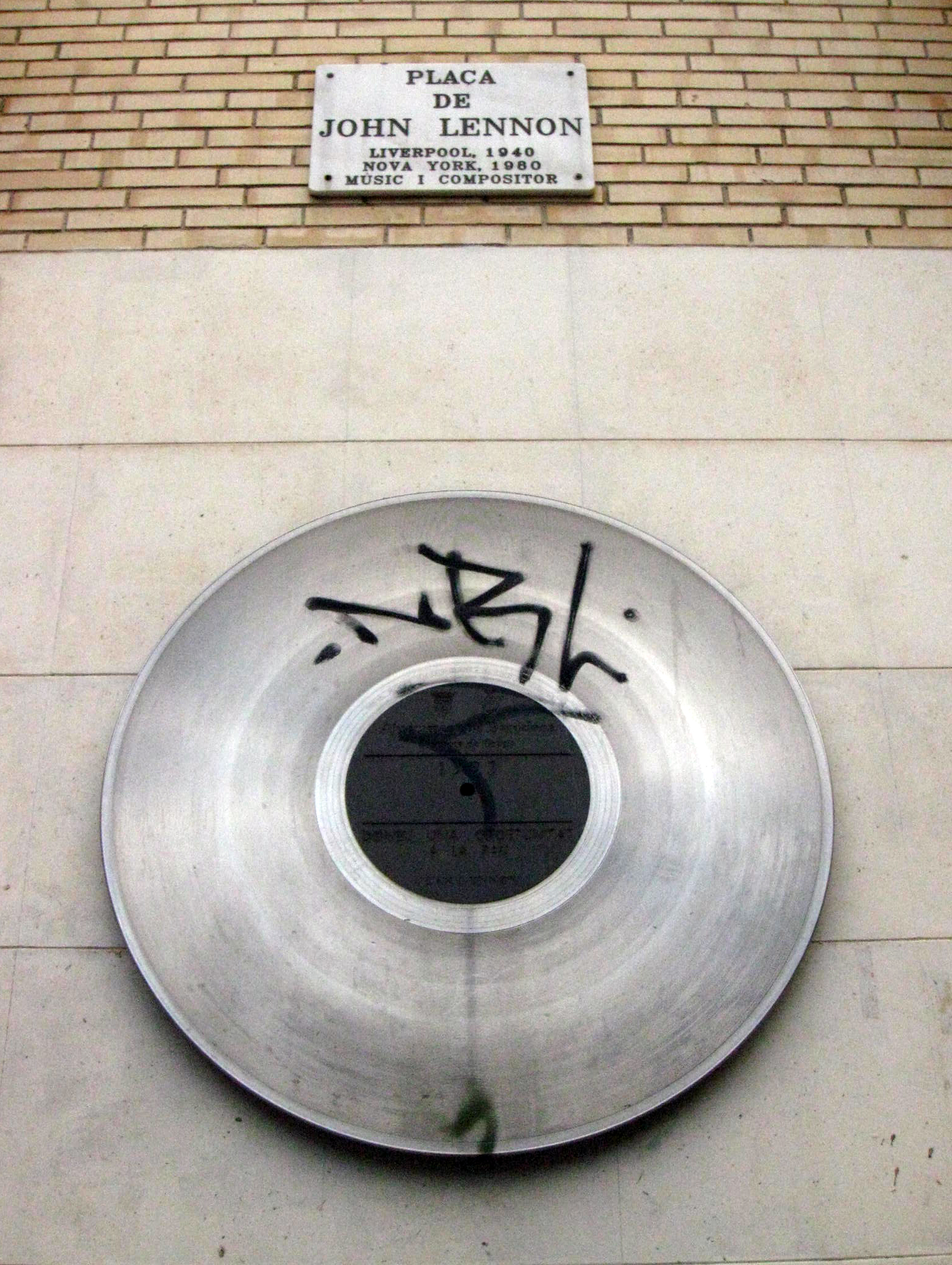 Record-shaped metal disc and marble street sign on a wall of Placa de John Lennon in Gracia, Barcelona